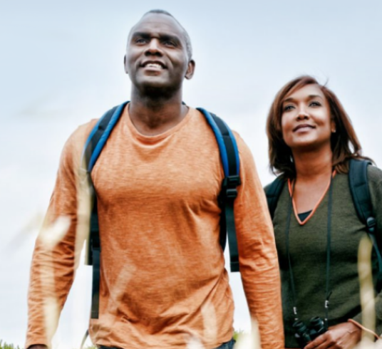 Man and woman smiling and walking with backpacks and binoculars