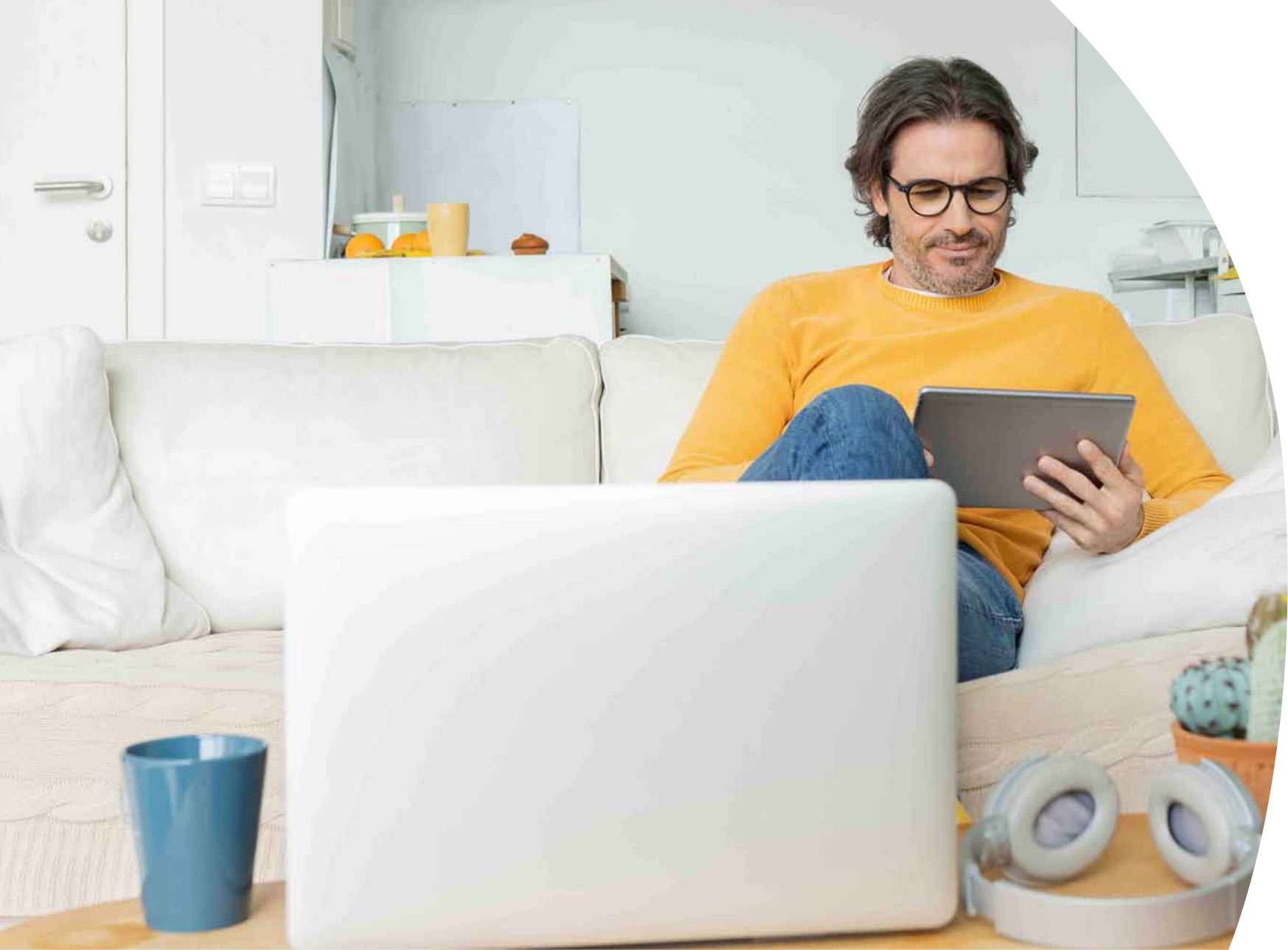 Man sitting on white couch and looking down at a tablet